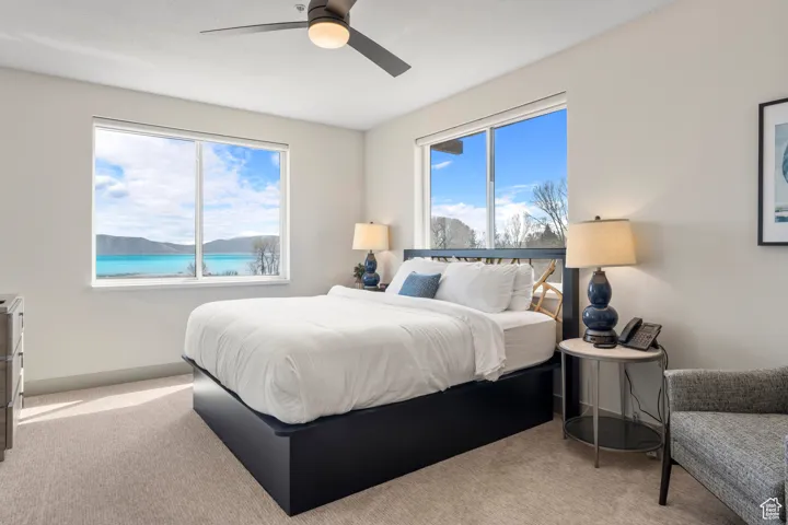 Carpeted bedroom with multiple windows, ceiling fan, and a water view