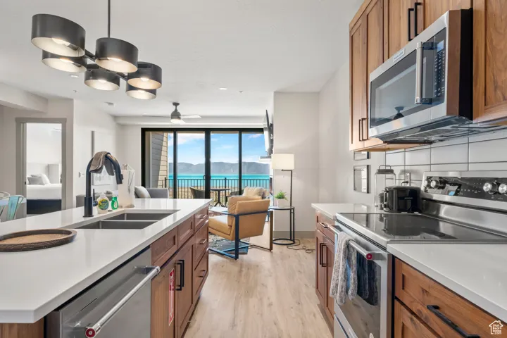 Kitchen with appliances with stainless steel finishes, a sink, brown cabinetry, open floor plan, and light wood-style floors