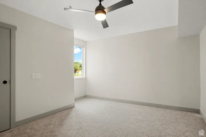 Carpeted empty room with a ceiling fan and baseboards