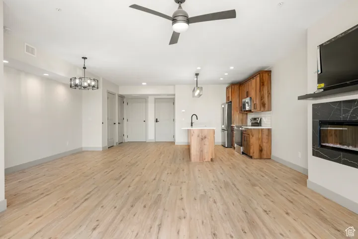 Unfurnished living room featuring light wood-type flooring, a ceiling fan, baseboards, a high end fireplace, and recessed lighting
