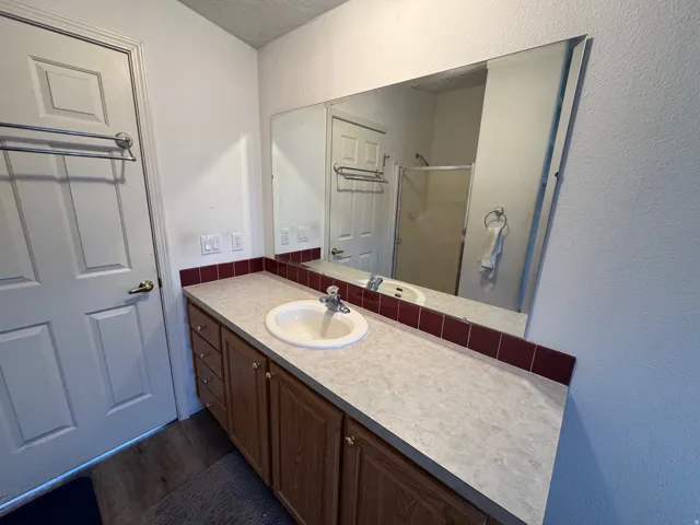 Full bathroom featuring a textured wall, vanity, a stall shower, and dark wood finished floors