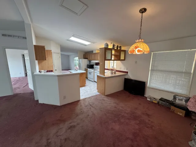 Kitchen with lofted ceiling, a peninsula, wood finish cabinetry, light colored carpet, and decorative light fixtures