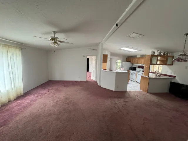 Unfurnished living room with light carpet, ceiling fan, and a textured ceiling
