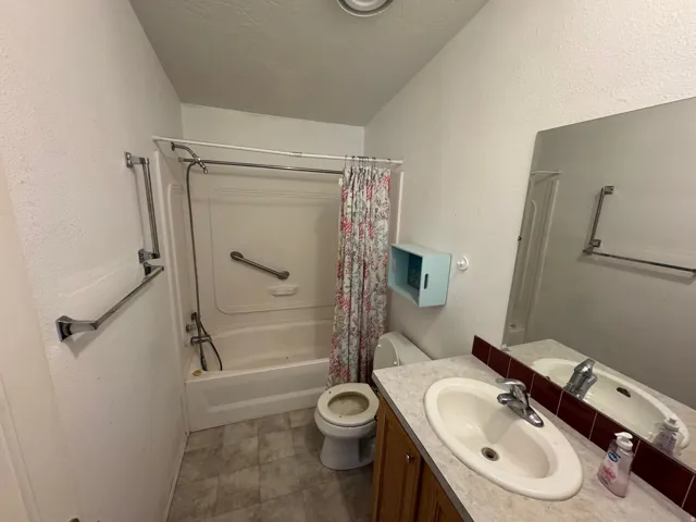 Full bathroom with vanity, shower / tub combo with curtain, a textured wall, and a textured ceiling
