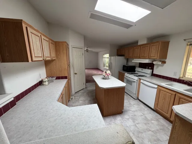 Kitchen featuring a kitchen island, light countertops, white appliances, and wood finish cabinetry
