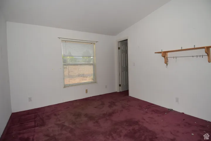 Unfurnished room featuring carpet and lofted ceiling