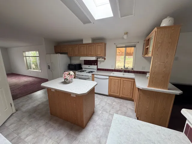 Kitchen with light countertops, a kitchen island, white appliances, and a skylight