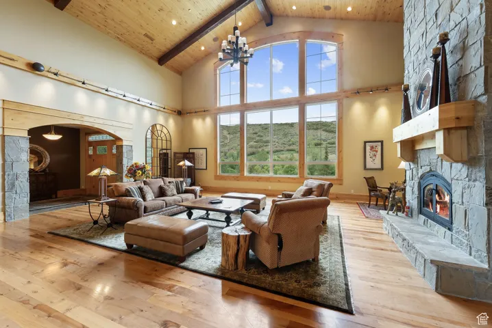 Living room with a stone fireplace, arched walkways, high vaulted ceiling, hardwood / wood-style flooring, and beamed ceiling