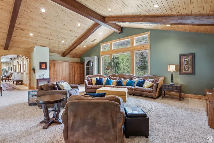 Carpeted living room with wood ceiling, beam ceiling, recessed lighting, arched walkways, and baseboards