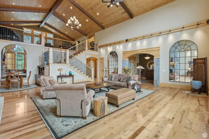 Living area featuring arched walkways, high vaulted ceiling, stairway, wood-type flooring, and beamed ceiling