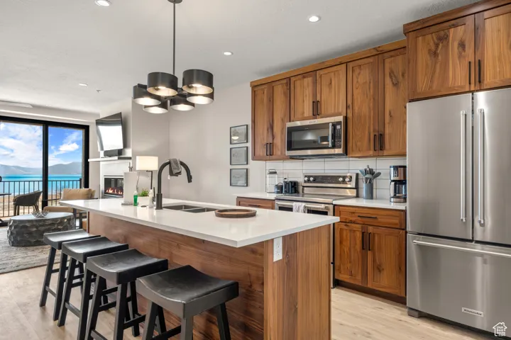 Kitchen featuring stainless steel appliances, a sink, light wood-type flooring, brown cabinetry, and recessed lighting