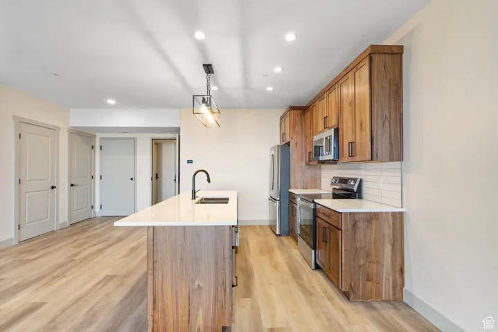 Kitchen with brown cabinetry, appliances with stainless steel finishes, a center island with sink, recessed lighting, and decorative backsplash
