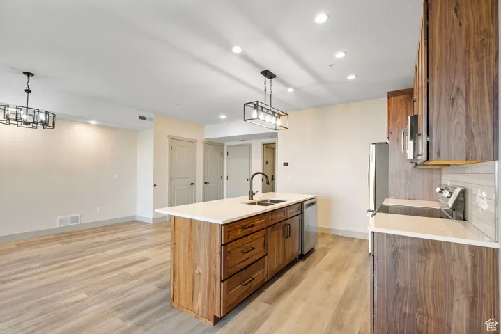 Kitchen with brown cabinets, recessed lighting, an island with sink, pendant lighting, and light wood-style flooring