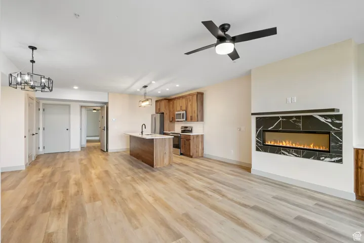 Kitchen featuring open floor plan, brown cabinets, an island with sink, hanging light fixtures, and a glass covered fireplace