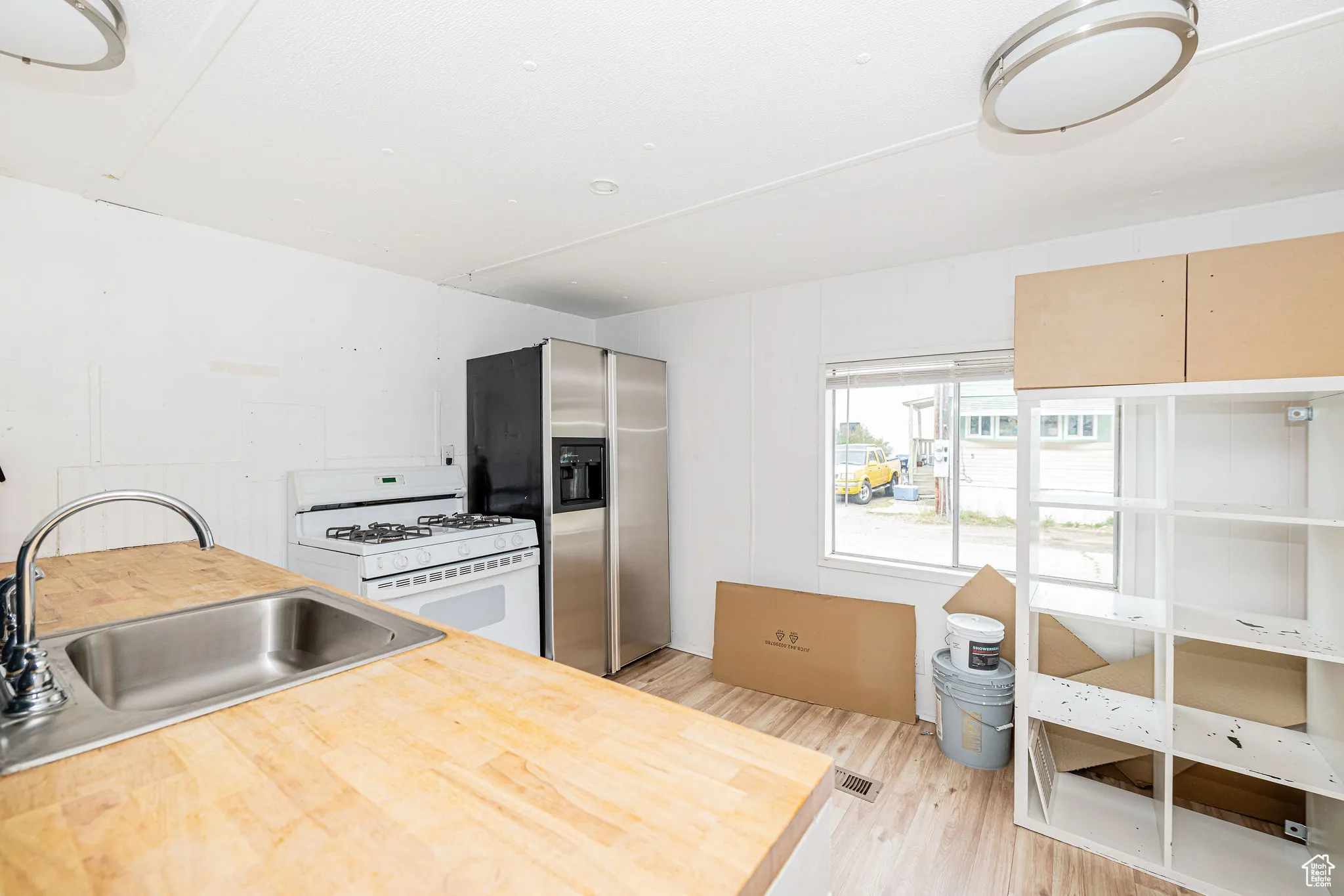 Kitchen featuring white gas stove, stainless steel refrigerator with ice dispenser, a sink, light wood-type flooring, and butcher block counters