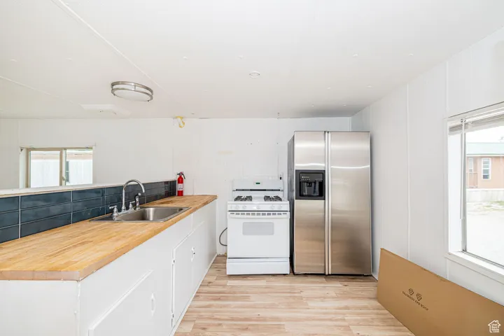 Kitchen with stainless steel refrigerator with ice dispenser, white range with gas stovetop, a sink, light wood-style flooring, and plenty of natural light
