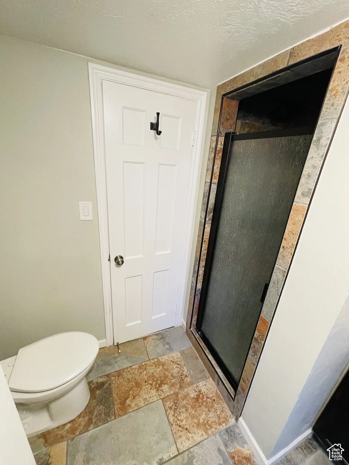 Bathroom featuring stone tile flooring, a stall shower, toilet, and baseboards