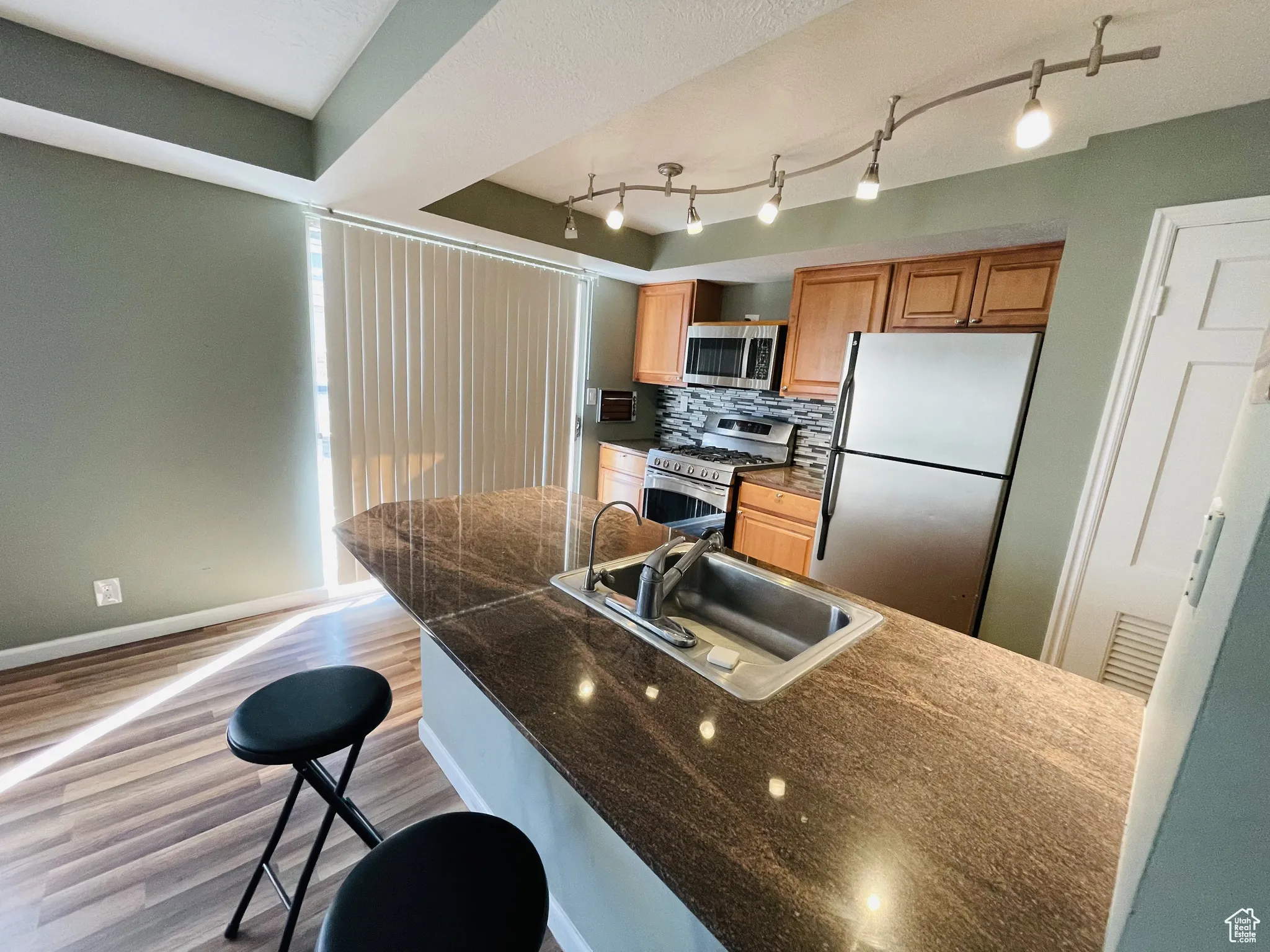 Kitchen featuring appliances with stainless steel finishes, a sink, light wood-type flooring, tasteful backsplash, and baseboards