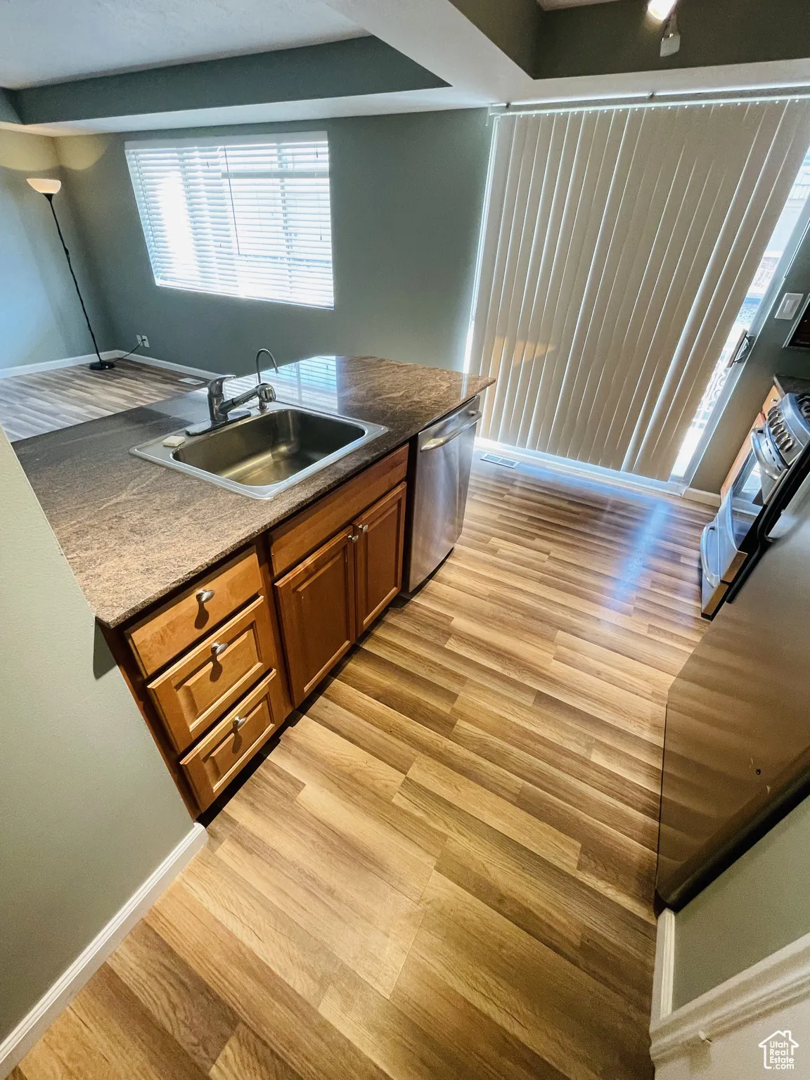 Kitchen featuring a sink, stainless steel dishwasher, light wood-type flooring, and brown cabinetry