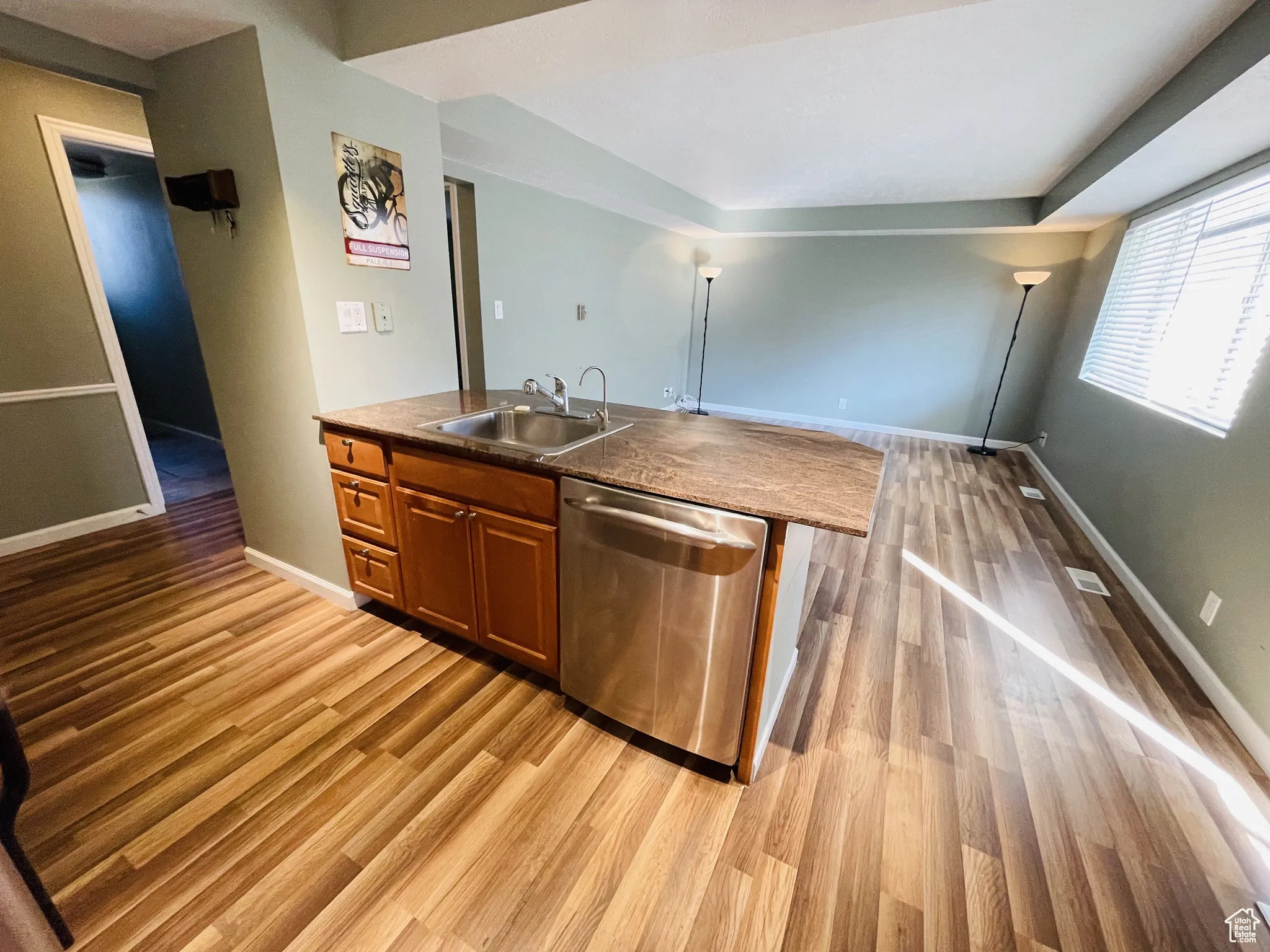 Kitchen with dishwasher, a sink, light wood-style flooring, brown cabinetry, and baseboards