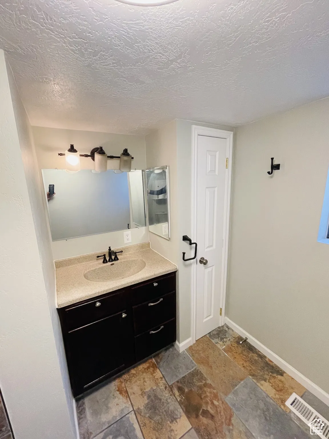 Bathroom with stone tile flooring, baseboards, vanity, and a textured ceiling