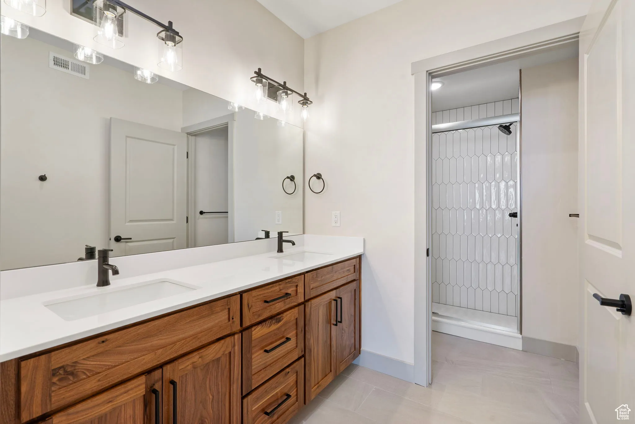 Full bathroom with a shower stall, double vanity, and light tile patterned floors