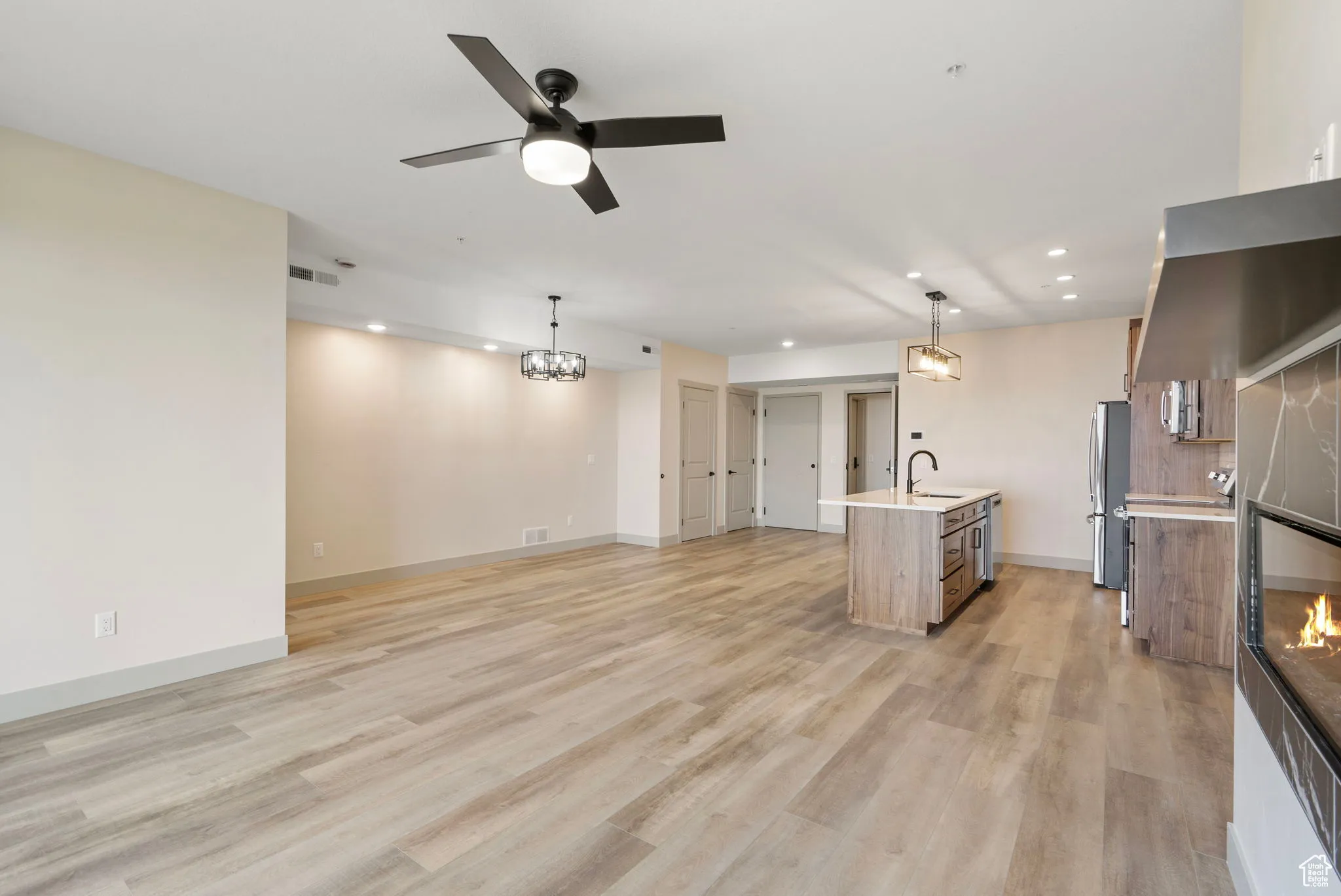 Unfurnished living room featuring recessed lighting, light wood-type flooring, a ceiling fan, a glass covered fireplace, and a chandelier