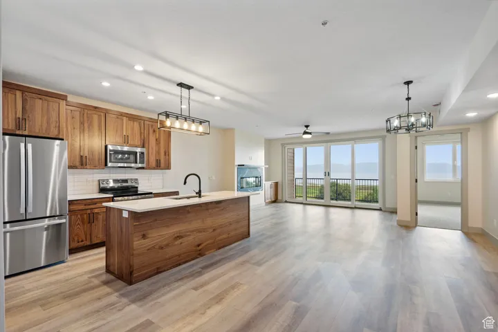 Kitchen with recessed lighting, brown cabinetry, stainless steel appliances, open floor plan, and decorative light fixtures