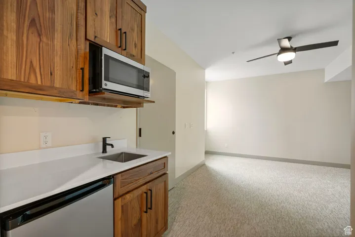 Kitchen with appliances with stainless steel finishes, brown cabinetry, light colored carpet, and light stone counters