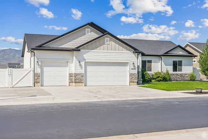 View of front facade featuring a garage, stone siding, concrete driveway, and a gate