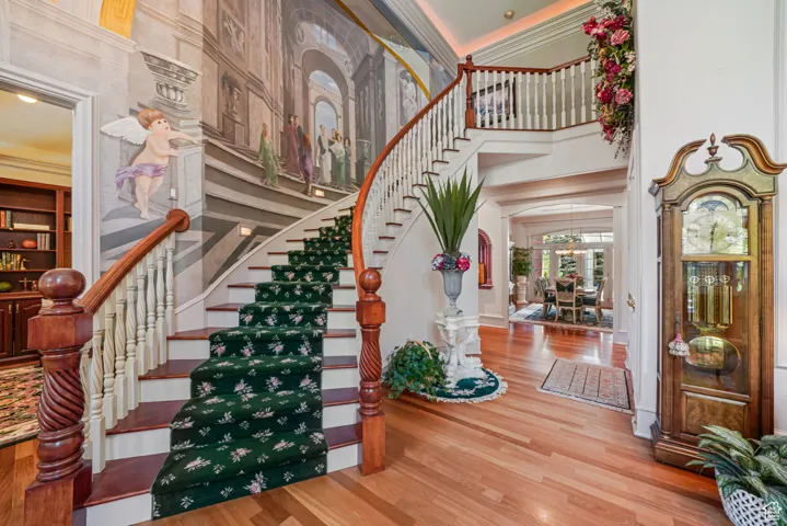 Entryway with arched walkways, a towering ceiling, stairway, wood finished floors, and ornamental molding