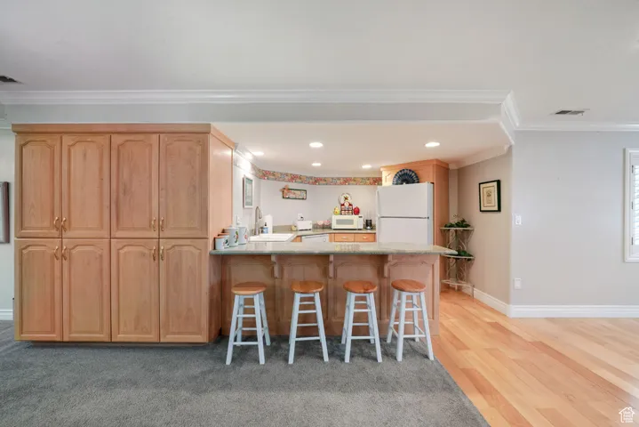 Kitchen featuring white appliances, crown molding, a kitchen bar, a peninsula, and light stone countertops
