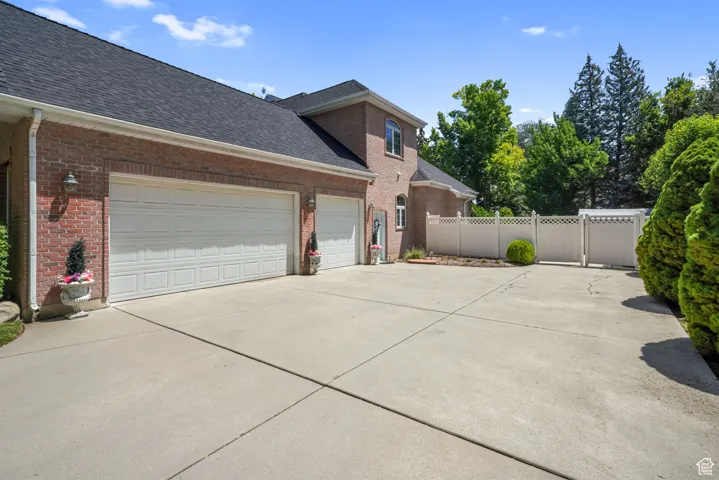 View of side of home with driveway, brick siding, a shingled roof, and an attached garage