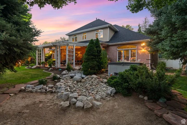 Back of property featuring a hot tub, a pergola, a shingled roof, brick siding, and a patio area
