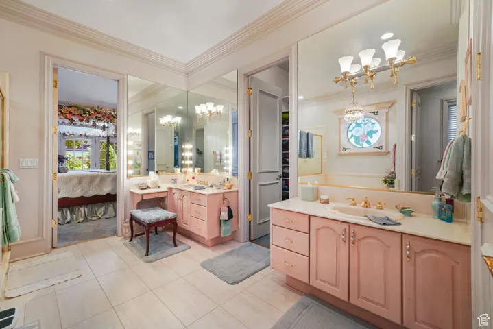 Ensuite bathroom featuring a chandelier, tile patterned floors, two vanities, and ornamental molding