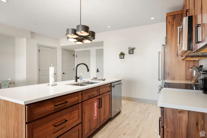 Kitchen with a sink, dishwasher, light countertops, a kitchen island with sink, and recessed lighting