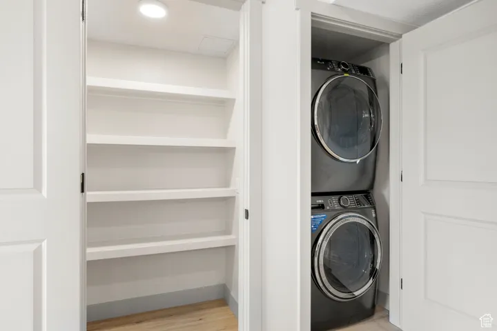 Laundry area with stacked washing machine and dryer and wood finished floors
