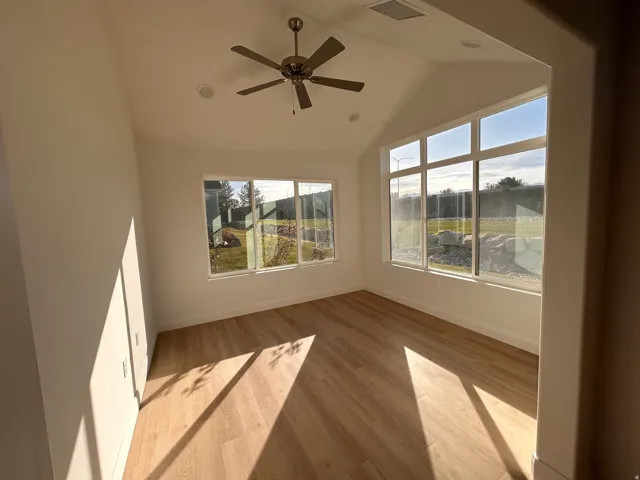 Empty room featuring wood finished floors, plenty of natural light, lofted ceiling, and a ceiling fan
