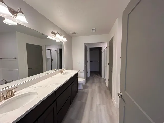 Bathroom featuring a walk in closet, double vanity, a stall shower, and light wood-type flooring