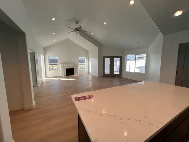 Kitchen with light wood-type flooring, high vaulted ceiling, open floor plan, a center island, and dark cabinets