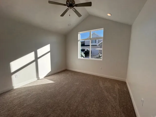 Carpeted spare room with ceiling fan and vaulted ceiling