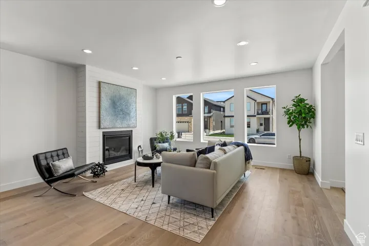 Living area with a large fireplace, light wood-type flooring, baseboards, and recessed lighting
