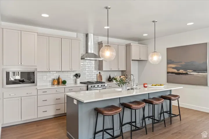 Kitchen featuring wall chimney exhaust hood, a sink, built in microwave, stainless steel range with gas cooktop, and wood finished floors