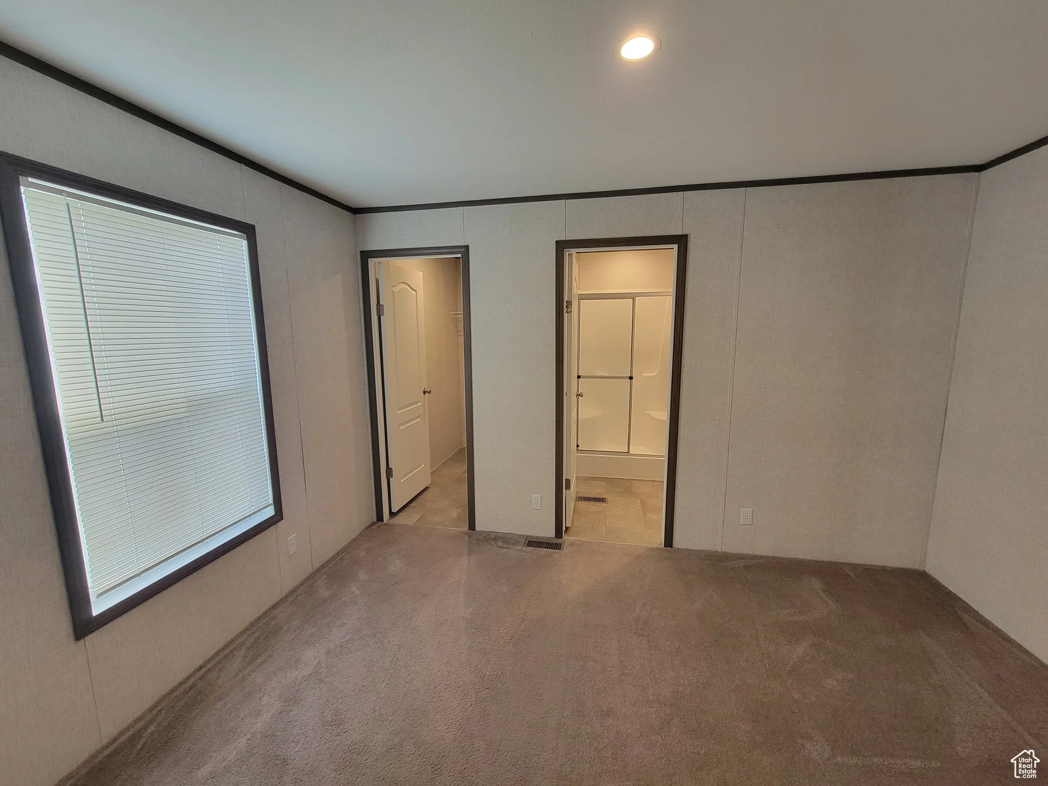 Unfurnished bedroom featuring crown molding, carpet floors, a decorative wall, and ensuite bath