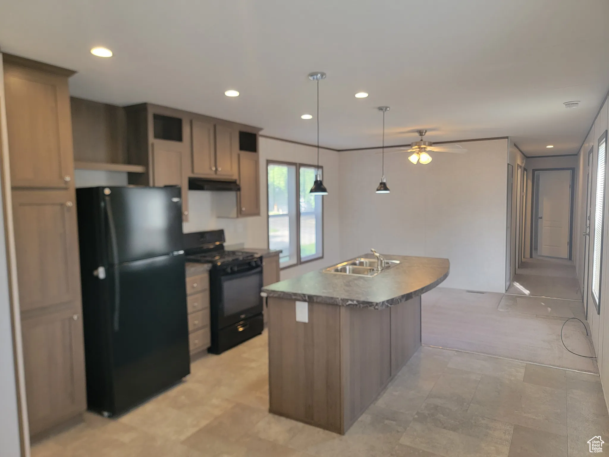 Kitchen featuring black appliances, under cabinet range hood, a sink, dark countertops, and an island with sink
