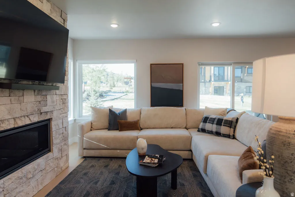 Living area featuring a stone-clad fireplace with a built-in linear firebox, large windows, recessed ceiling lighting, and wood-finish flooring