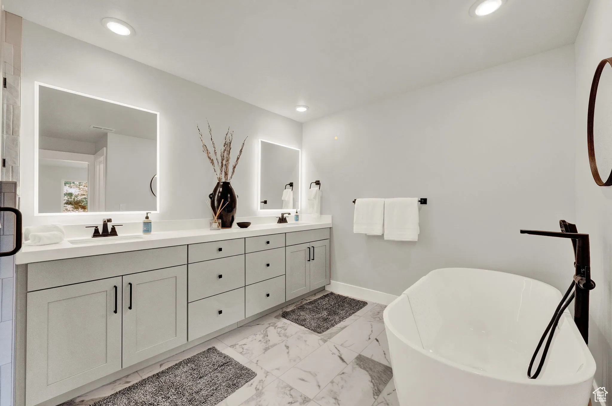 Full bath featuring double vanity, a soaking tub, marble look tiles, recessed lighting, and baseboards
