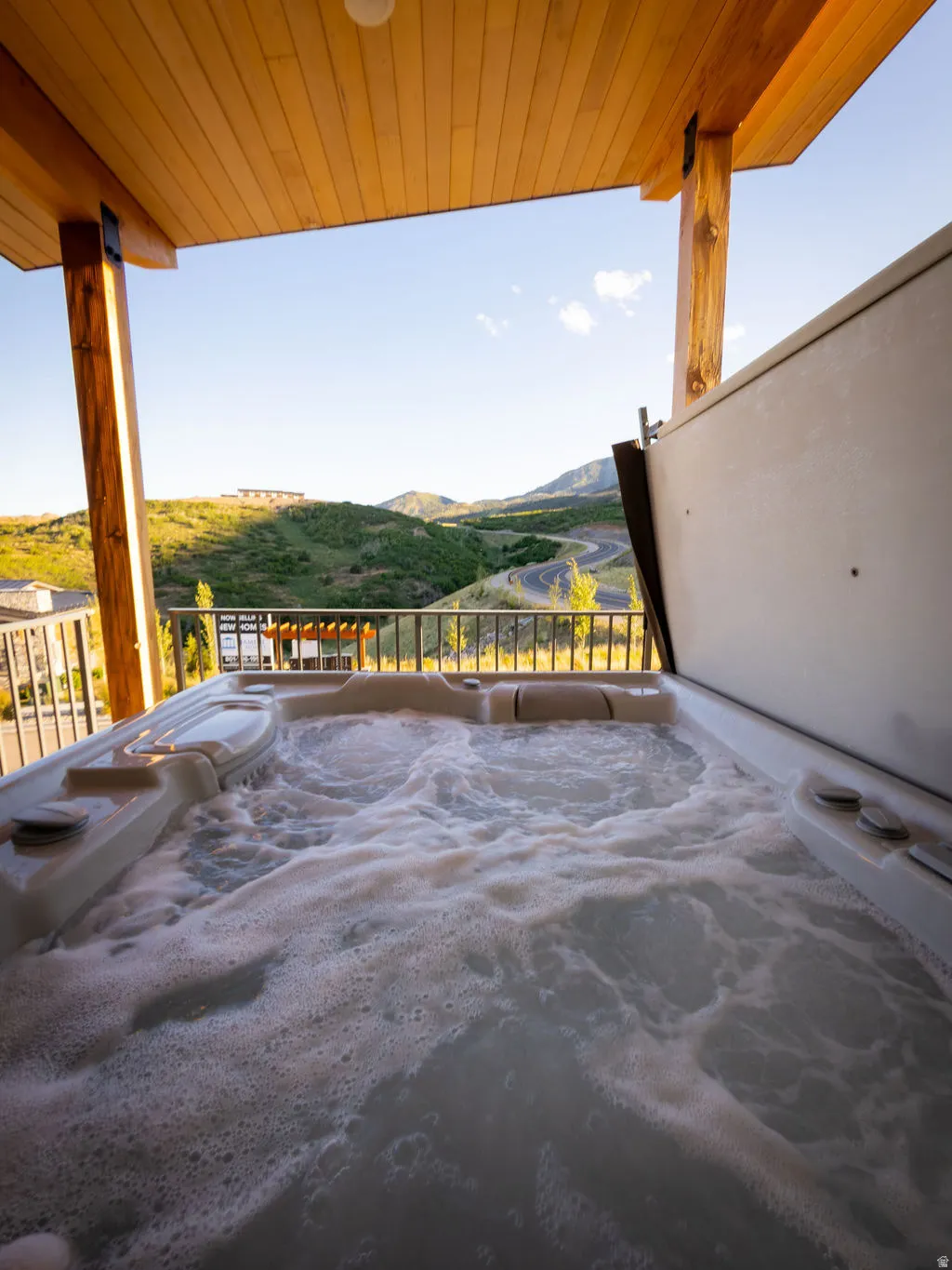 Outdoor hot tub featuring a slatted wood ceiling, exposed wood beams, and a metal railing