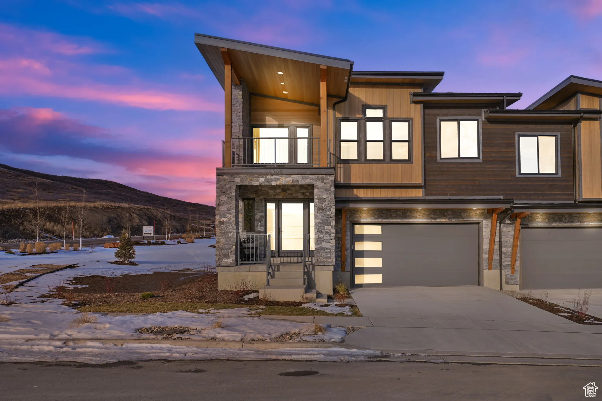 Contemporary home featuring a balcony, a mountain view, stone siding, an attached garage, and driveway