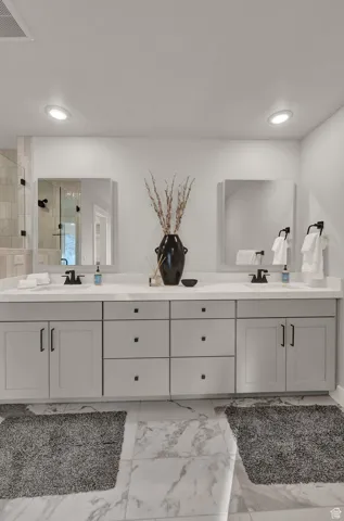 Full bathroom featuring a tile shower, double vanity, marble look tiles, and recessed lighting